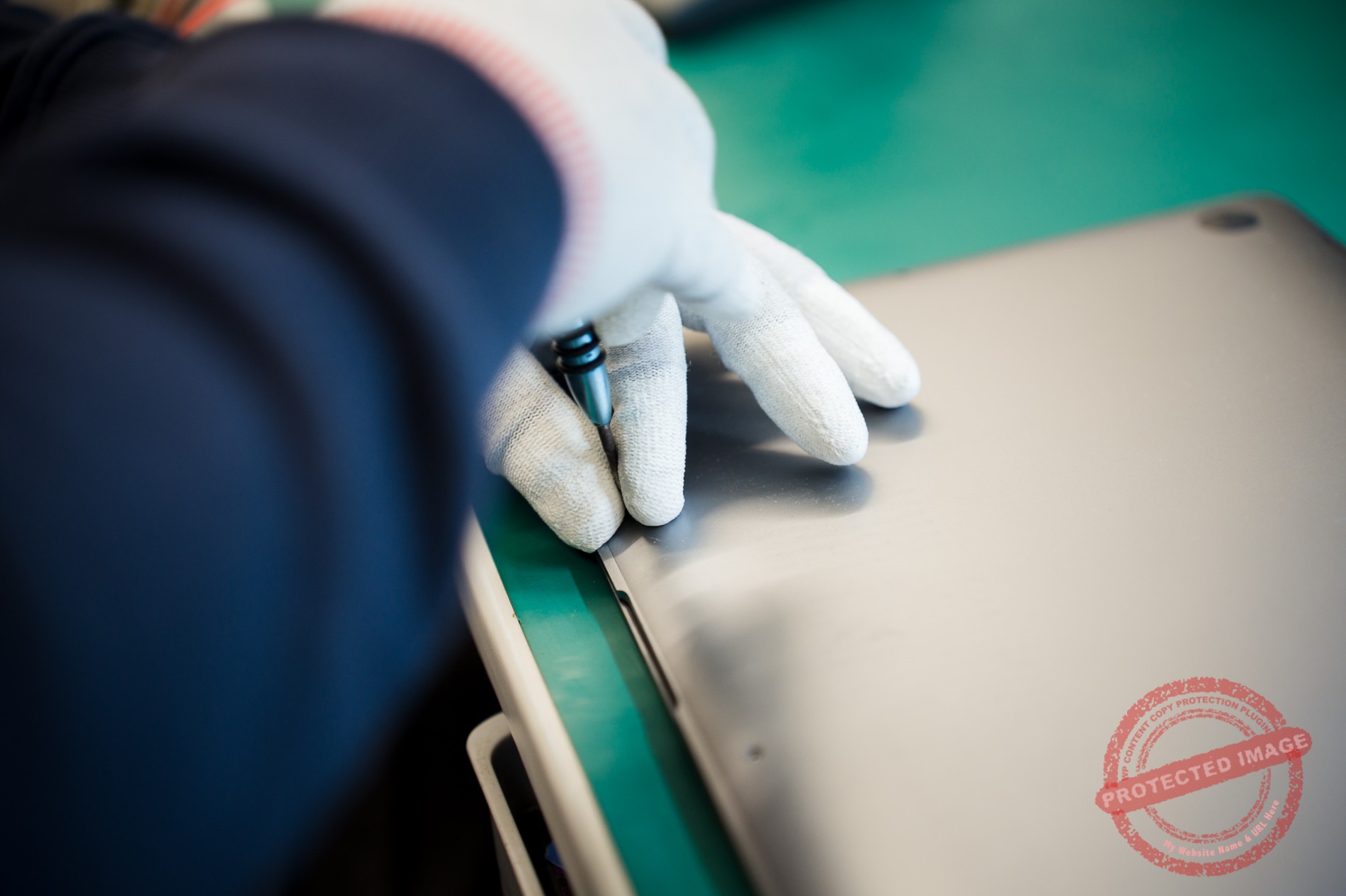 Gloved technician opening MacBook case with pry tool on workbench